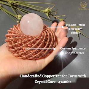May include: A handcrafted copper tensor torus with a crystal core. The torus is made of coiled copper wire and holds a spherical, translucent rose quartz crystal. Text on the image reads "432 MHz - Main Frequency outside" and "Custom Frequency inside the center."