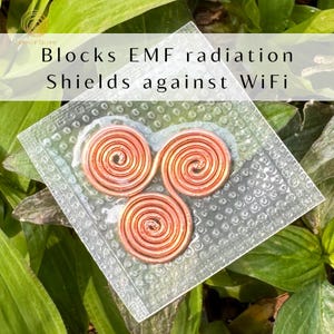 May include: A clear, sealed package containing three copper spiral coils. The package is set against a backdrop of green leaves. Text on the package reads: "Blocks EMF radiation Shields against WiFi."
