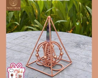 Könnte beinhalten: Ein kupferfarbener Orgon-Generator in Pyramidenform mit einem zentralen Kristall. Die Pyramide hat ein geometrisches Design mit einem Kristall an der Spitze. Der Text "THE ONLY SHOP OF TENSORSTORE" steht oben. Der Text "RANDOM GIFTS" steht unten.