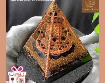 Puede incluir: Una pirámide de energía orgónica con detalles de alambre de cobre, piedras negras e inclusiones doradas. La pirámide se asienta sobre una base gris oscuro. El texto "THE ONLY SHOP OF TENSORSTORE" es visible en la parte superior. La imagen también incluye el texto "RANDOM GIFTS".