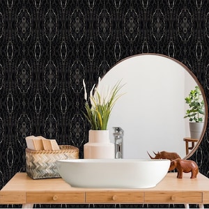 Może przedstawiać: Czarno-złota tapeta w geometryczny wzór z białą ceramiczną umywalką, drewnianym blatem z dwoma szufladami, okrągłym lustrem, rośliną w doniczce i dwiema drewnianymi figurkami słoni.