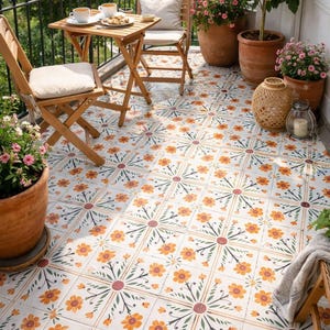 May include: A balcony with wooden furniture, including a small table and chairs, set on patterned tiles. Potted plants with pink flowers and a lemon tree add colour. A black metal railing surrounds the space.