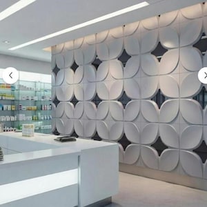 Könnte beinhalten: Innenraum einer modernen Apotheke mit weißem Tresen und dekorativer Wand mit sich wiederholendem Blütenblattmuster. Regale mit Produkten sind im Hintergrund sichtbar, mit einer hellen Decke.