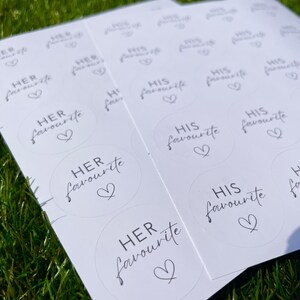 May include: A sheet of white stickers with black text and a heart design. The stickers say "HER favourite" and "HIS favourite".
