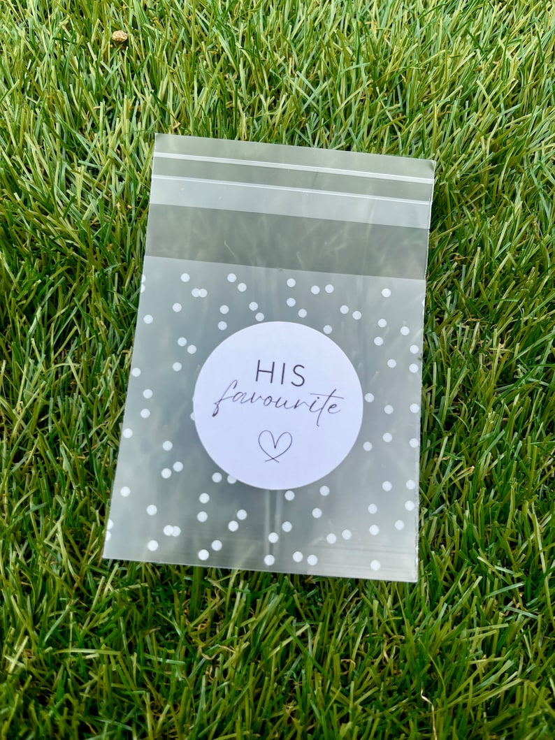May include: A clear plastic bag with a white polka dot pattern. The bag has a sticker on it that says "HIS favourite" with a heart symbol.