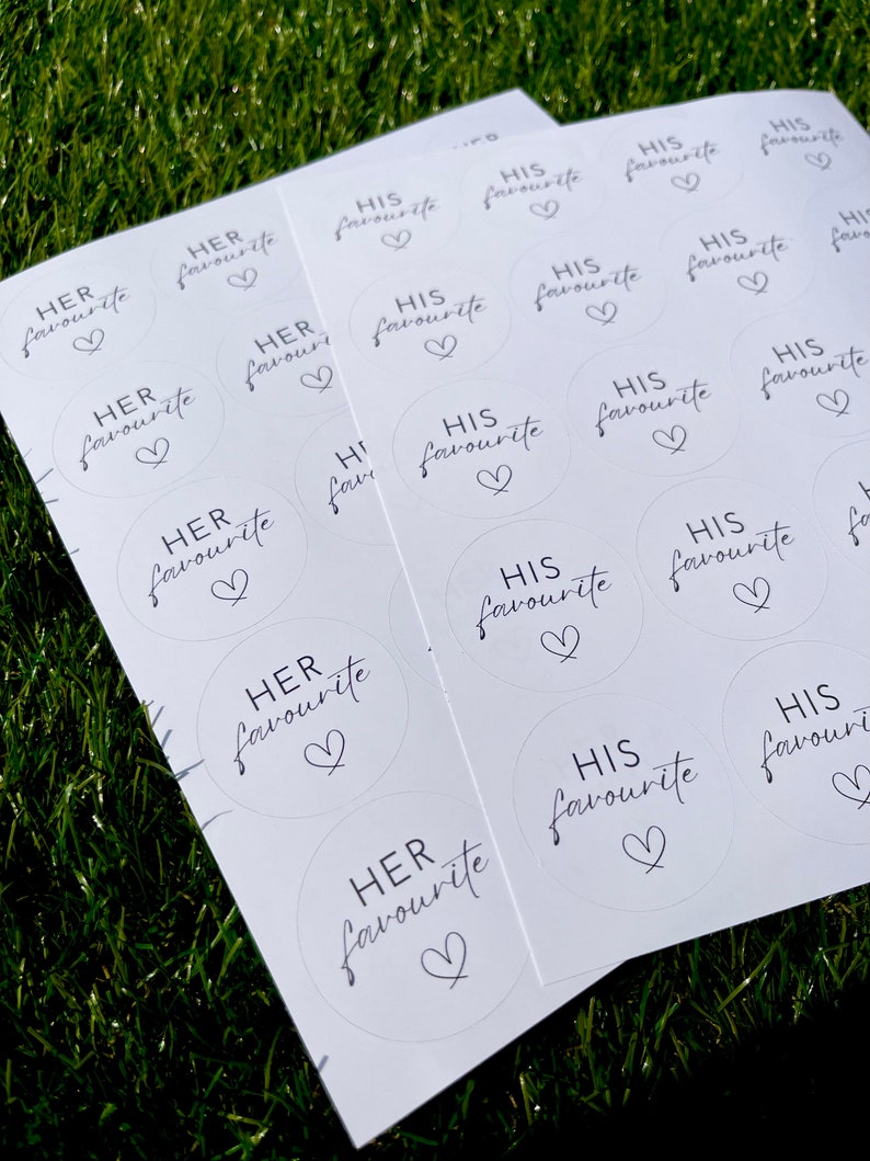 May include: A sheet of white paper with round stickers printed with the text "His favourite" and "Her favourite" in black script with a heart symbol.