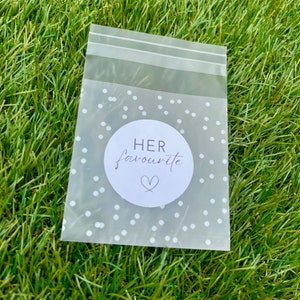 May include: A clear plastic bag with a white polka dot pattern and a white circle sticker that says "HER favourite" with a heart symbol.