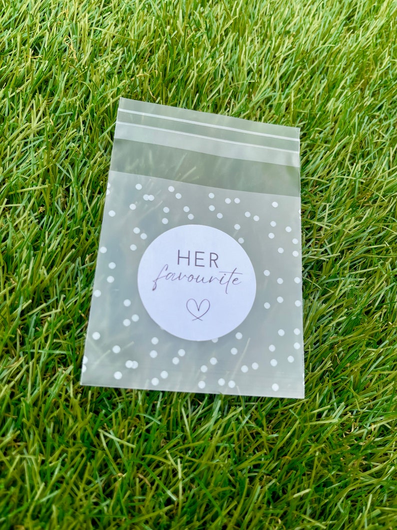 May include: A clear plastic bag with a white polka dot pattern and a white circle sticker that says "HER favourite" with a heart symbol.