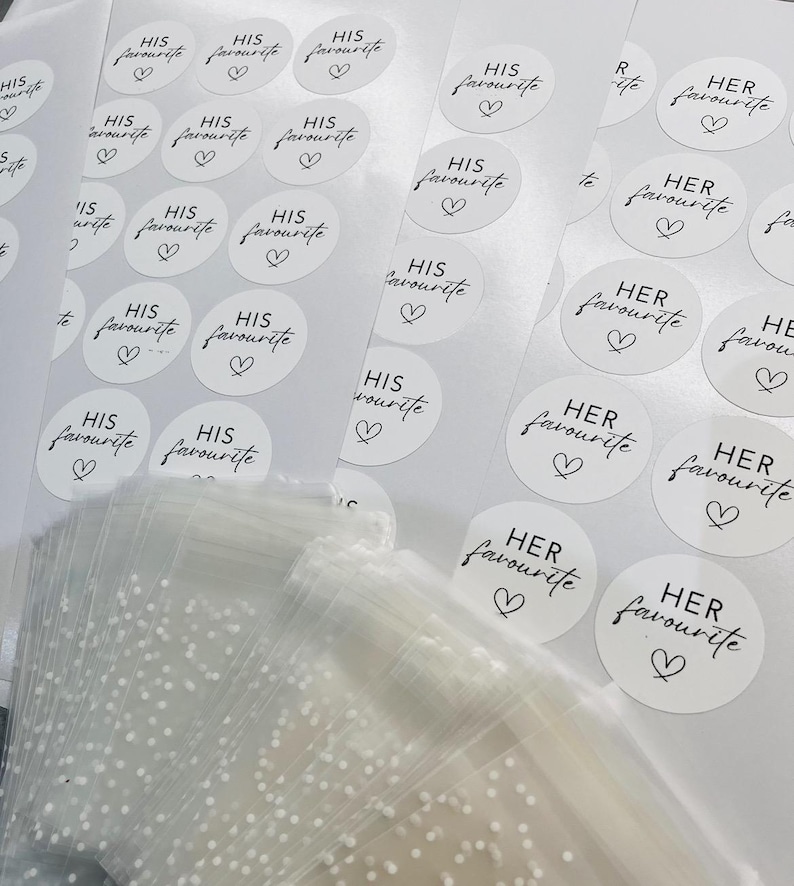 May include: A sheet of white stickers with black text that reads "His favourite" and "Her favourite" with a small heart symbol. The stickers are arranged in rows and columns.