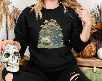 Könnte beinhalten: Ein schwarzes Sweatshirt mit einem Aufdruck eines Igels, der von Pilzen umgeben ist. Der Igel ist braun und weiß und die Pilze sind in verschiedenen Brauntönen und Weiß.