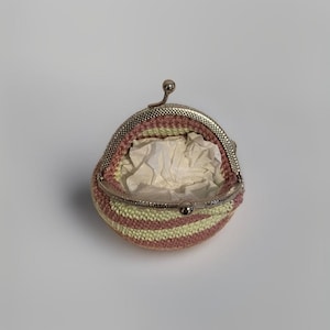 Può includere: Un piccolo porta monete all'uncinetto con un motivo a righe rosa e giallo e una chiusura argentata.