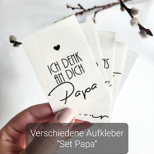 Könnte beinhalten: Ein Set weißer Aufkleber mit schwarzem Text, der "Ich denk an Dich Papa" mit einem kleinen schwarzen Herzen lautet. Der Text "Set Papa" steht unter den Aufklebern.