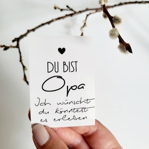 Könnte beinhalten: Eine weiße Karte mit schwarzem Text, der "Du bist Opa. Ich wünscht du könntest es erleben." lautet. Die Karte hat oben ein kleines schwarzes Herz.