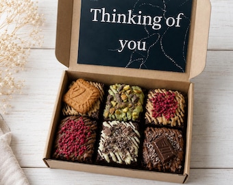 Könnte beinhalten: Eine Geschenkbox aus Pappe mit sechs dekorierten Brownies. Die Brownies sind mit Nüssen, getrockneten Beeren und einem Keks belegt. Eine Karte mit dem Text "Thinking of you" befindet sich in der Box.