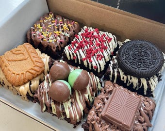 May include: A cardboard gift box containing six square chocolate brownies with various toppings, including colorful sprinkles, dried raspberries, a sandwich cookie, a biscuit, mint chocolate spheres, and a milk chocolate square, with the text Birthday.