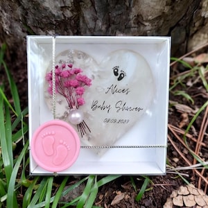 Pu&ograve; includere: Un segnaposto per baby shower con un design a forma di cuore con la scritta "Alice's Baby Shower" e la data 08.09.2023. Il cuore &egrave; decorato con fiori rosa e una perla, ed &egrave; presentato in una scatola bianca con un sigillo di cera rosa.