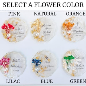 Op de afbeelding: Een selectie van gepersonaliseerde hars onderzetters met gedroogde bloemen en goudblad accenten. Elke onderzetter heeft een andere bloemkleur: roze, naturel, oranje, lila, blauw en groen. Tekst bevat namen, data en evenementen zoals dopen en bruidsdouches.