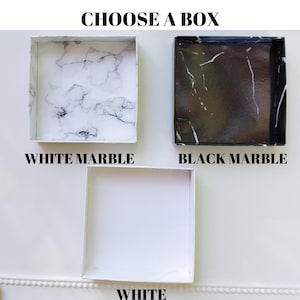 Pu&ograve; includere: Tre scatole quadrate con diversi design. La scatola superiore ha un motivo a marmo bianco, la scatola centrale ha un motivo a marmo nero e la scatola inferiore &egrave; bianca. Il testo in alto dice "CHOOSE A BOX". Il testo sotto ogni scatola indica il design: "WHITE MARBLE", "BLACK MARBLE" e "WHITE".