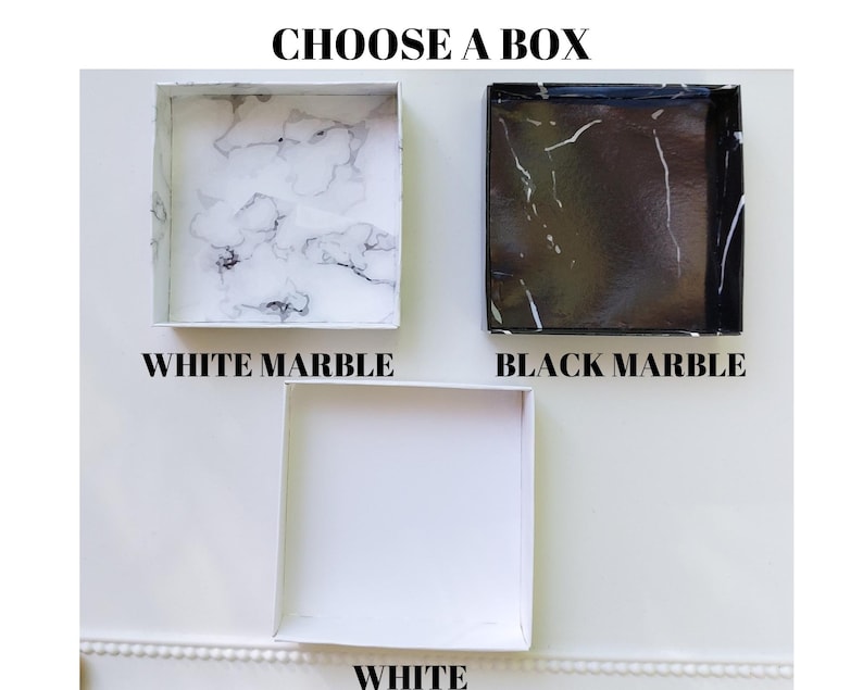 Pu&ograve; includere: Tre scatole quadrate con diversi design. La scatola superiore ha un motivo a marmo bianco, la scatola centrale ha un motivo a marmo nero e la scatola inferiore &egrave; bianca. Il testo in alto dice "CHOOSE A BOX". Il testo sotto ogni scatola indica il design: "WHITE MARBLE", "BLACK MARBLE" e "WHITE".