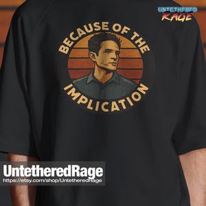May include: Black t-shirt featuring a circular graphic with a man's portrait and the text "BECAUSE OF THE IMPLICATION." The graphic has a retro sunset design. The shirt also has the text "UntetheredRage" and a website address.