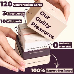 Hands lifting the lid off the beige Our Guilty Pleasures box with purple lettering to reveal multiple stacks of conversation cards inside, showing light pink, beige, and dark purple card backs. The image highlights: 120 conversation cards, 3 flirty levels, 10 wildcards, 0 awkward moments, 100% expert-designed.
