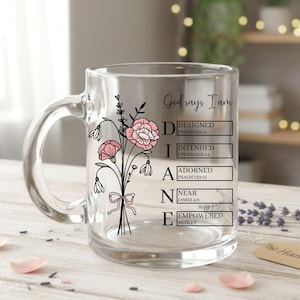 May include: A clear glass mug with a handle, featuring a floral design and the words "God says I am" followed by "Designed, Intended, Adorned, Near, Empowered." The mug has a bouquet of pink flowers and black line art.