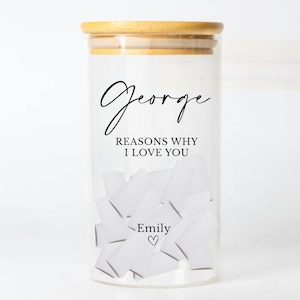 May include: A clear glass jar with a bamboo lid, filled with folded white paper notes. The jar is labeled "George" and "Reasons Why I Love You," with "Emily" and a heart symbol below. A thoughtful gift.