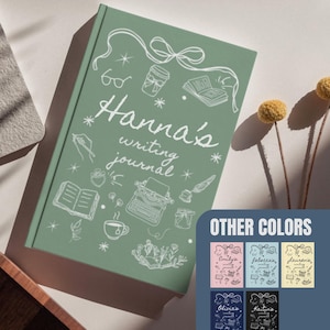 May include: A sage green journal with the text "Hanna's writing journal" in white script. The cover features white illustrations of a coffee cup, glasses, a typewriter, and other writing-related icons. Additional color options are shown.