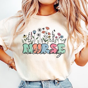 May include: A cream colored t-shirt with a floral design and the text "NURSE mother baby" in colorful letters.