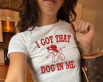 May include: White cropped t-shirt with a red graphic of a balloon dog wearing a cowboy hat. The text "I got that dog in me" is printed in red on the shirt.