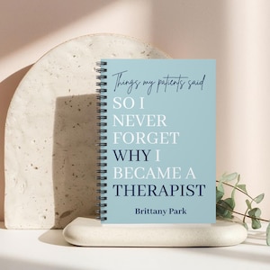 May include: A light blue spiral-bound notebook with dark blue and white text that reads: Things my patients said SO I NEVER FORGET WHY I BECAME A THERAPIST Brittany Park. The notebook features a black metal coil binding along the left side.
