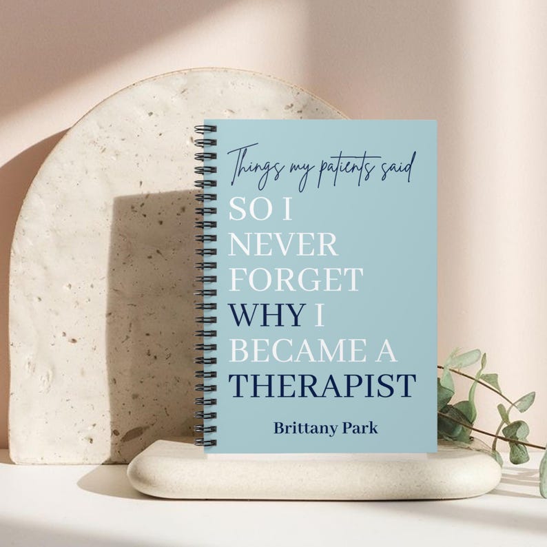 May include: A light blue spiral-bound notebook with dark blue and white text that reads: Things my patients said SO I NEVER FORGET WHY I BECAME A THERAPIST Brittany Park. The notebook features a black metal coil binding along the left side.