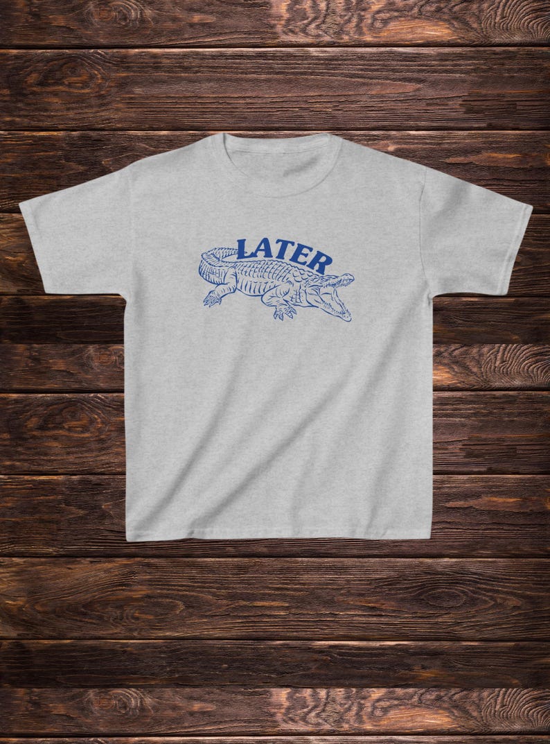 May include: A light grey t-shirt with a blue alligator graphic and the word "LATER" printed above it.