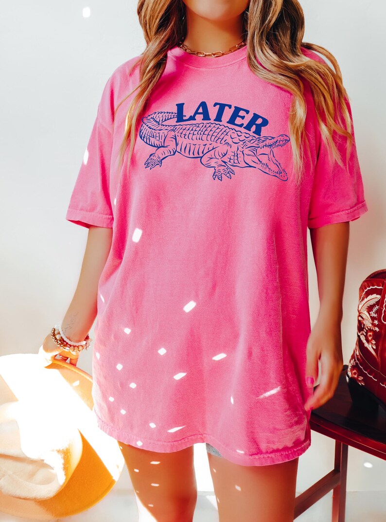 May include: A pink t-shirt with a blue alligator graphic and the word "LATER" printed on it.