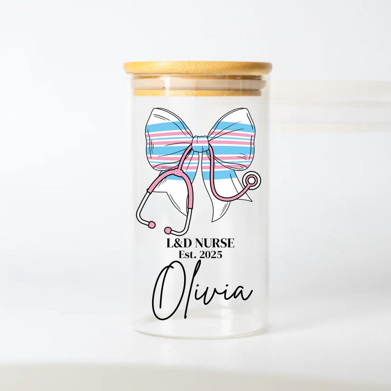 May include: A clear glass jar with a bamboo lid, featuring a pink stethoscope and a blue and pink striped bow. The jar has the text "L&D NURSE Est. 2025 Olivia" printed on it.