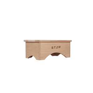 May include: A wooden step stool with a rounded top and a cutout design on the bottom. The stool is made of light wood and has the word "STEP" engraved on the top.