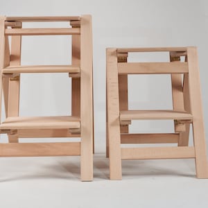 May include: Two wooden step stools, one taller than the other, both with three steps. The stools are made of light wood and have a natural finish.