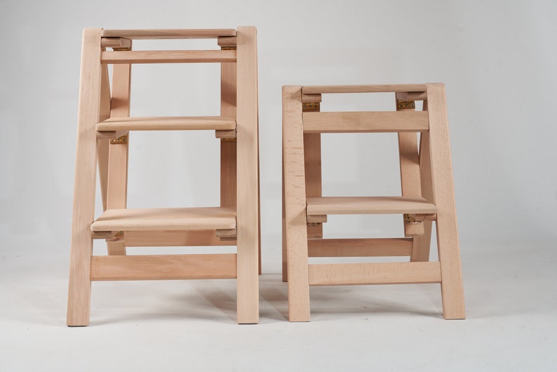 May include: Two wooden step stools, one taller than the other, both with three steps. The stools are made of light wood and have a natural finish.
