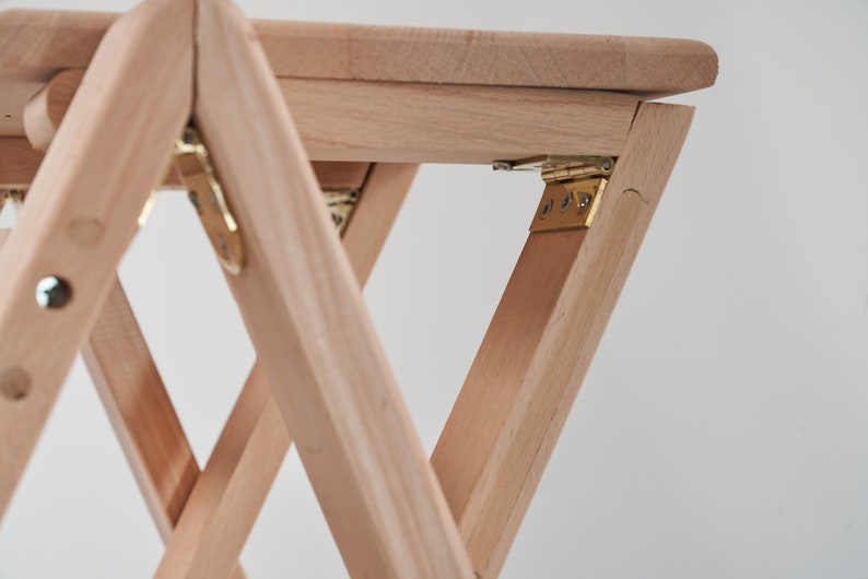 May include: A wooden folding stool with brass hinges. The stool is made of light wood and has a simple design.