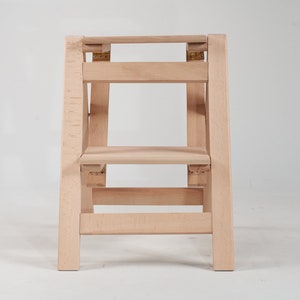 May include: A wooden step stool with two steps. The stool is made of light wood and has a simple design.