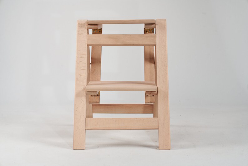 May include: A wooden step stool with two steps. The stool is made of light wood and has a simple design.