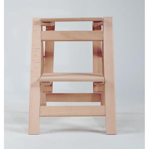 May include: A natural wood step stool with two steps. The stool is made of solid wood and has a simple, functional design.