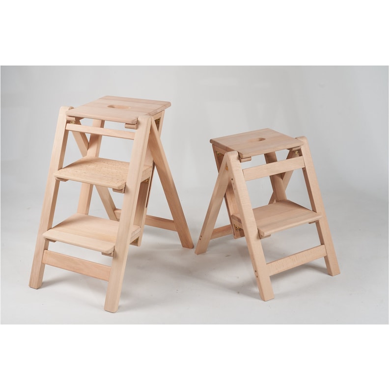May include: Two wooden step stools, one with three steps and one with two steps. Both stools are made of light wood and have a simple, modern design.