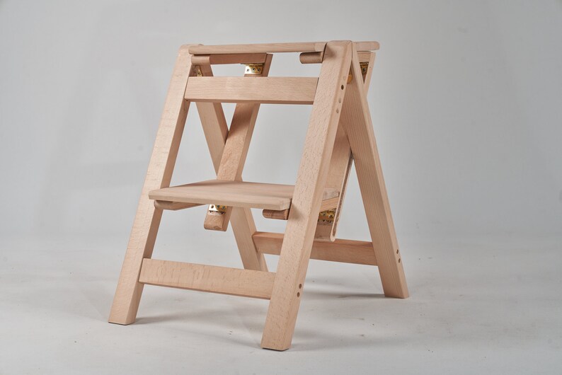 May include: A light wood step stool with two steps and a folding design. The stool is made of natural wood and has a simple, minimalist design.