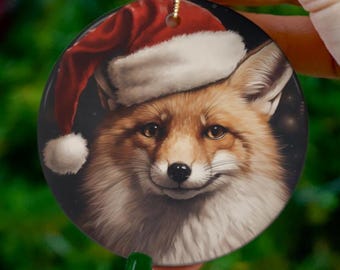 Peut inclure: Ornement de Noël rond représentant un renard portant un bonnet de Père Noël. Le renard a un pelage brun et blanc, un nez noir et des yeux foncés. Le bonnet de Père Noël est rouge avec une bordure blanche et un pompon blanc. L'ornement a une ficelle dorée pour l'accrocher.