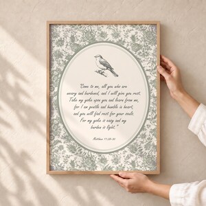 Può includere: Una stampa artistica da parete incorniciata con uno sfondo a motivo floreale verde salvia e un ovale centrale contenente l'illustrazione di un piccolo uccello e il testo: Come to me, all you who are weary and burdened, and I will give you rest. Matthew 11:28-30.