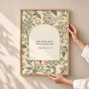 May include: A rectangular framed print featuring a cream-colored arched center panel surrounded by a botanical pattern of green leaves and muted pink and blue flowers. The text reads: YOUR CUSTOM QUOTE, POEM OR SAYING HERE. Scripture Verse 6:21-25.