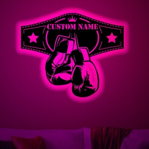 Peut inclure: Une silhouette noire de gants de boxe suspendus à une ceinture de champion avec des étoiles et le texte "CUSTOM NAME". L'arrière-plan est rose vif.