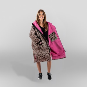 Puede incluir: Una bata con estampado de leopardo con interior rosa y cremallera negra. La bata tiene capucha y un bolsillo con diseño de estampado de leopardo. La persona lleva zapatillas deportivas negras.