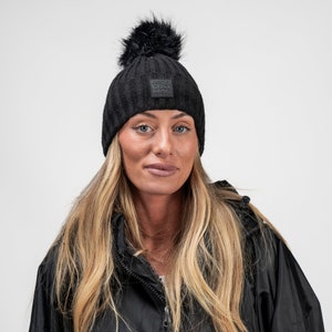 以下が含まれることがあります： ポンポンが付いた黒いニット帽。帽子には「Cool Mag」と書かれた小さな黒い正方形のロゴがあります。